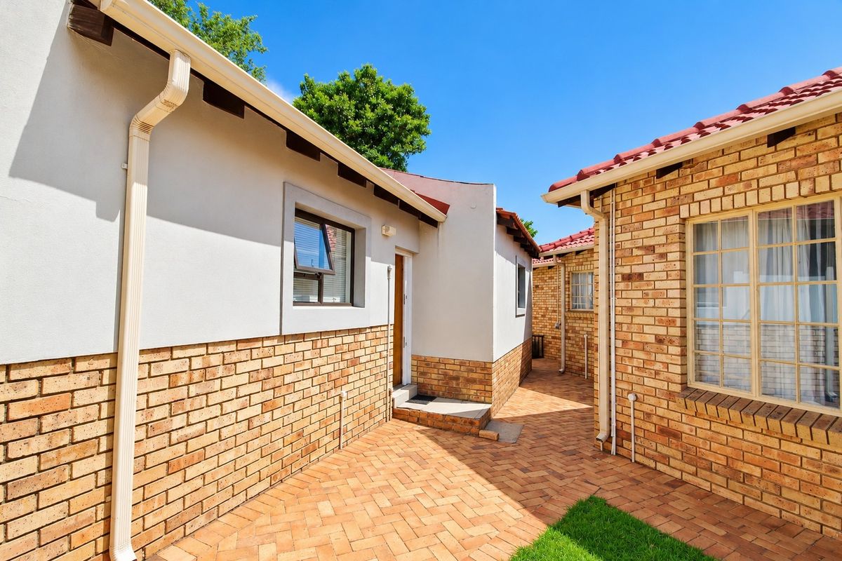A well-maintained rear courtyard featuring face brick and plastered walls, paved flooring, and clean architectural lines between two sections of the house.
