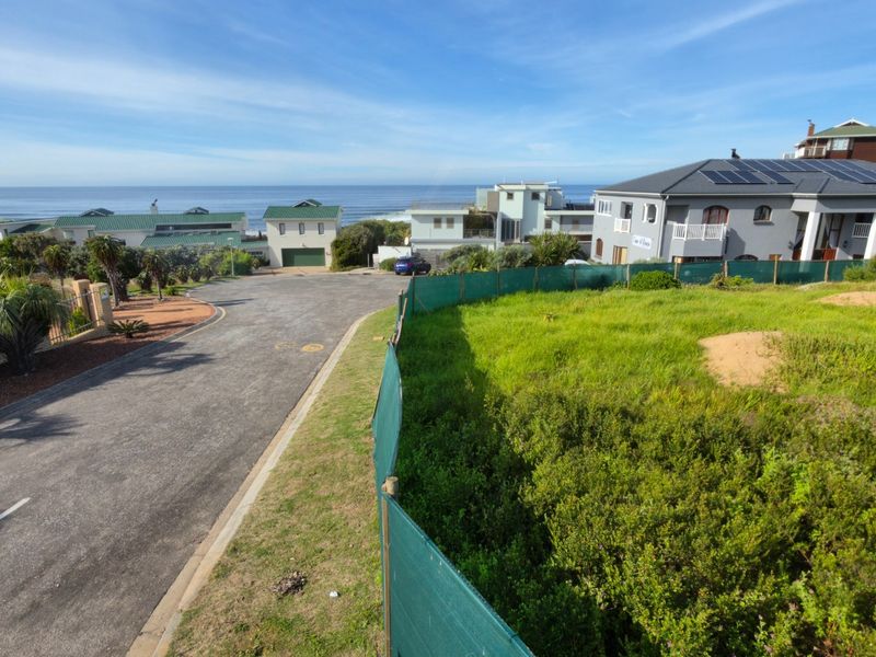 An elevated view of a vacant residential plot situated in a coastal neighborhood, featuring adjacent paved road access and established surrounding properties.