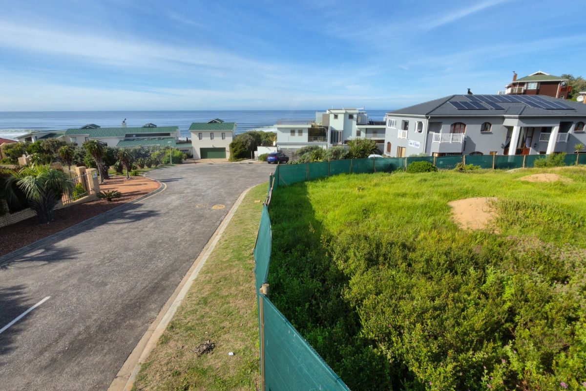 An elevated view of a vacant residential plot situated in a coastal neighborhood, featuring adjacent paved road access and established surrounding properties.