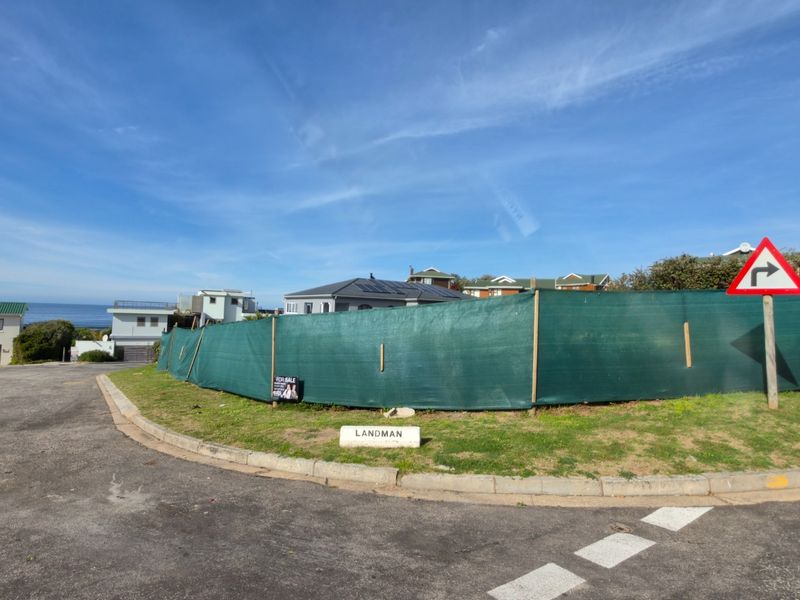 A vacant residential plot situated on a corner lot, enclosed by temporary green shade cloth fencing with street access.