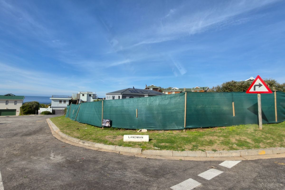 A vacant residential plot situated on a corner lot, enclosed by temporary green shade cloth fencing with street access.