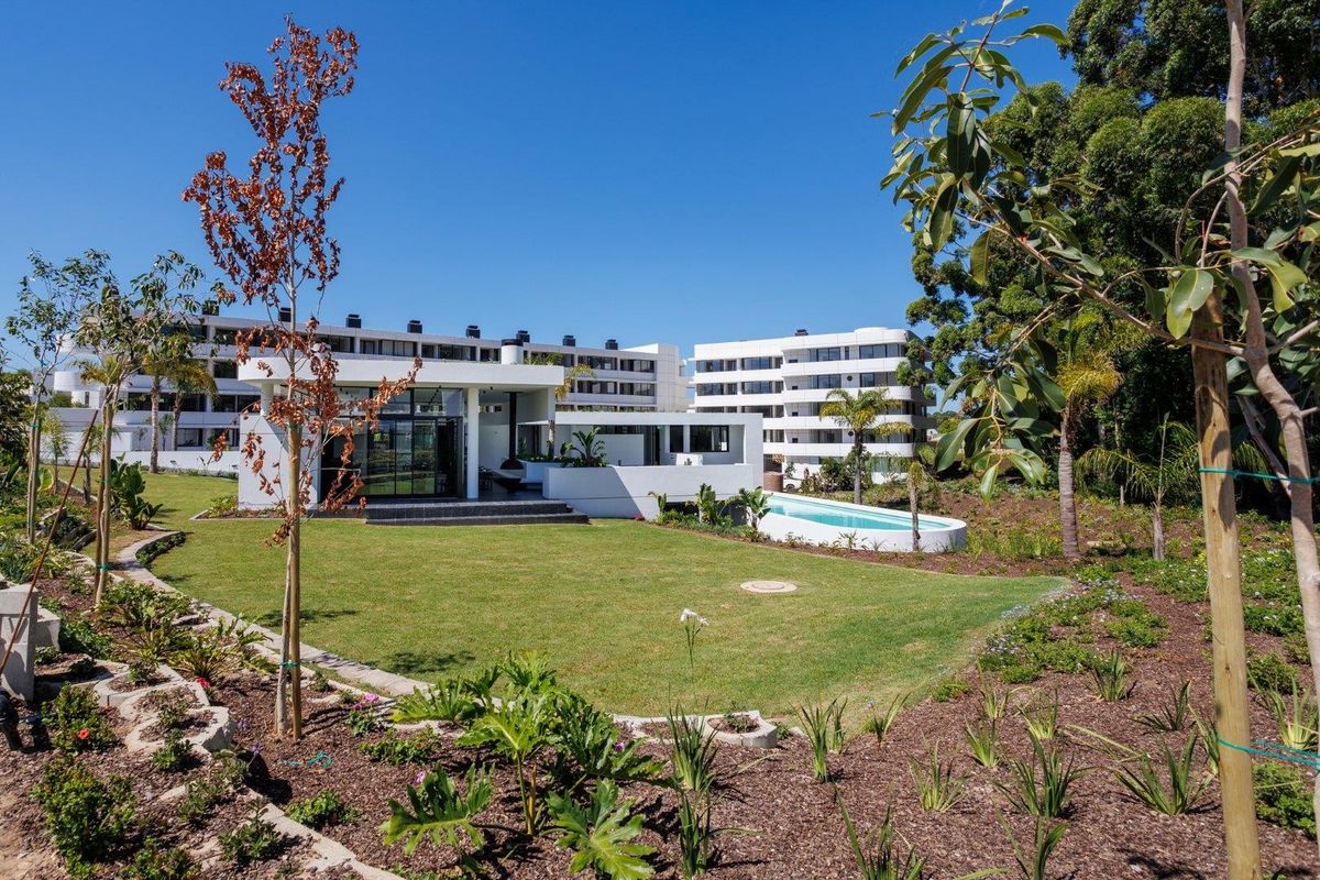 A well-maintained rear exterior view featuring a landscaped garden, a modern patio area, and a private swimming pool set against a contemporary apartment building.