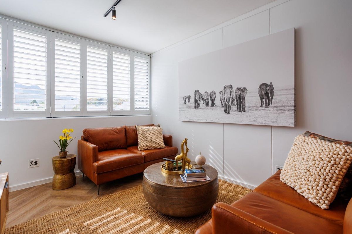 A bright and modern living room featuring elegant herringbone flooring, plantation shutters, and contemporary track lighting, creating a warm and inviting atmosphere.