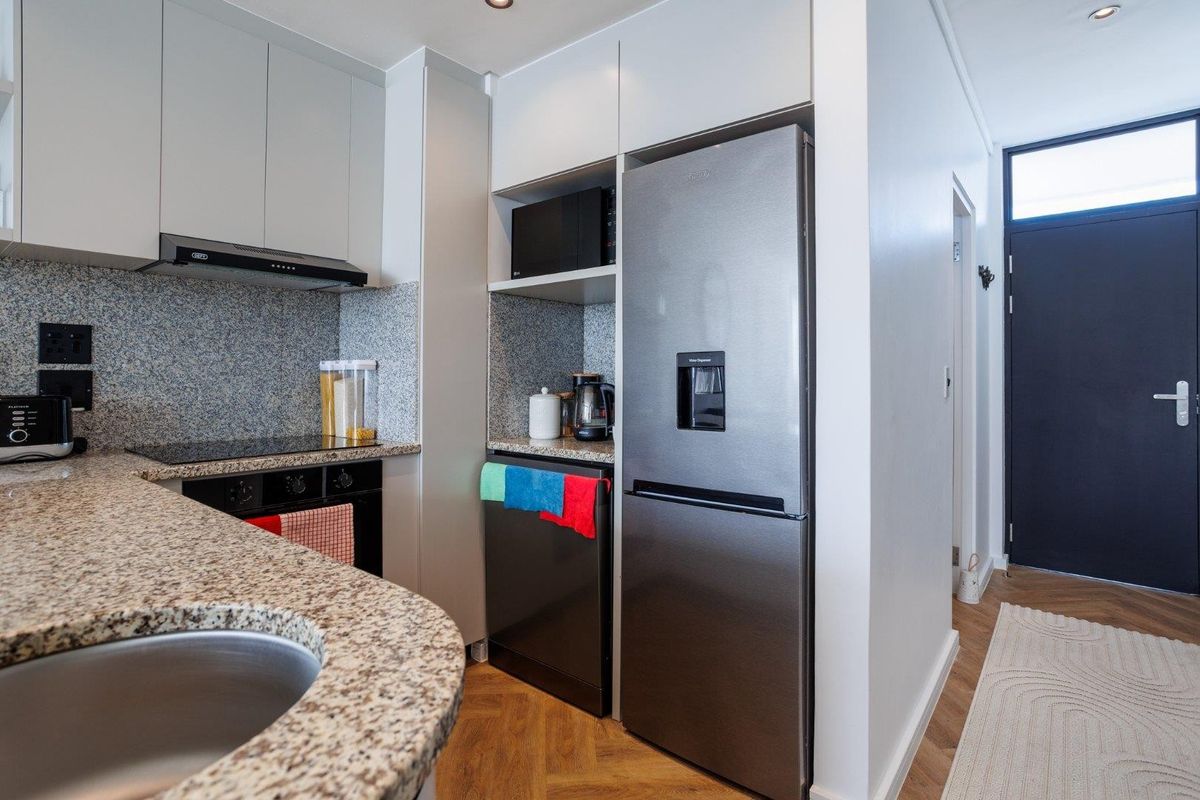 Modern kitchen featuring granite countertops, built-in oven, electric hob, extractor fan, and sleek cabinetry, complemented by stylish herringbone flooring.