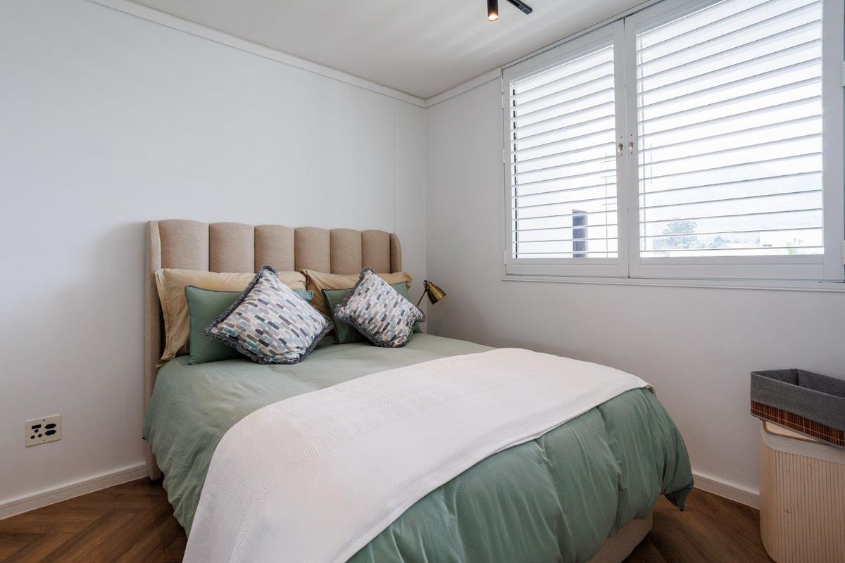 A well-maintained bedroom featuring herringbone flooring, white plantation shutters, and a modern ceiling spotlight, offering a clean and comfortable living space.
