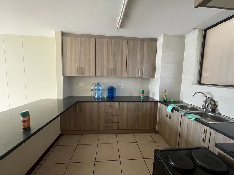 A functional kitchen featuring wood-look laminate cabinetry, granite countertops, and a double stainless steel sink with tiled splashbacks and flooring.