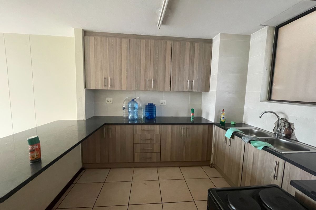 A functional kitchen featuring wood-look laminate cabinetry, granite countertops, and a double stainless steel sink with tiled splashbacks and flooring.