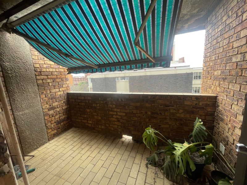 A private balcony featuring face brick walls, tiled flooring, and a retractable striped awning, offering a functional outdoor space with potential for improvement.