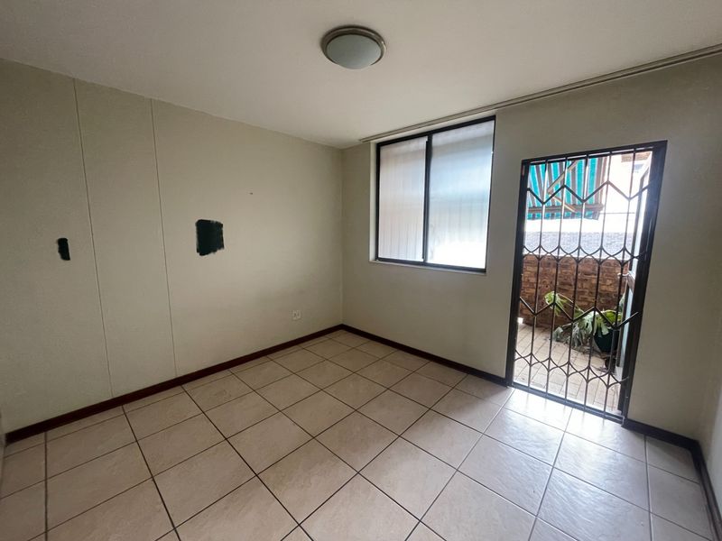 An empty bedroom featuring tiled flooring, a security gate leading to a balcony, and a window, requiring minor cosmetic wall repairs.