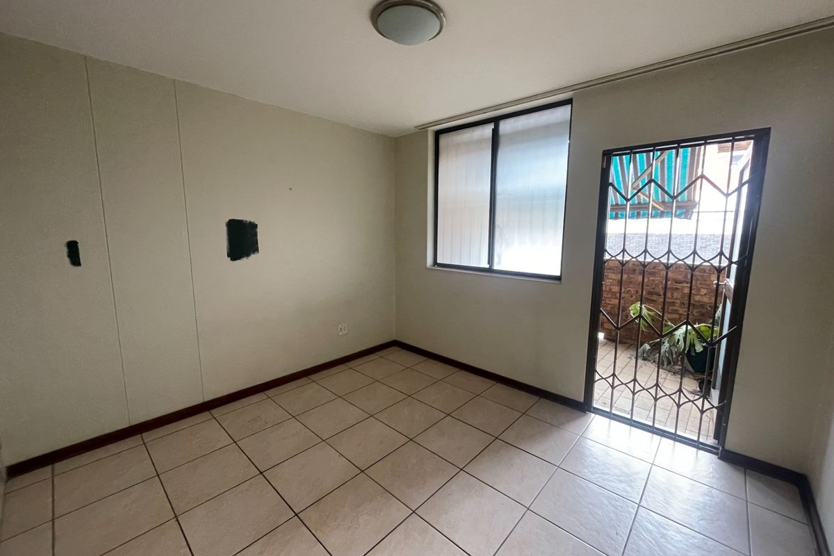 An empty bedroom featuring tiled flooring, a security gate leading to a balcony, and a window, requiring minor cosmetic wall repairs.