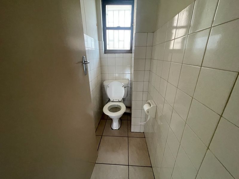 A compact, functional bathroom featuring tiled walls and flooring, equipped with a standard toilet and a window with security bars.