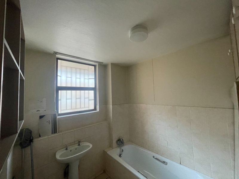 A functional bathroom featuring a pedestal washbasin, bathtub, and tiled splashback, with built-in shelving and security bars on the window.