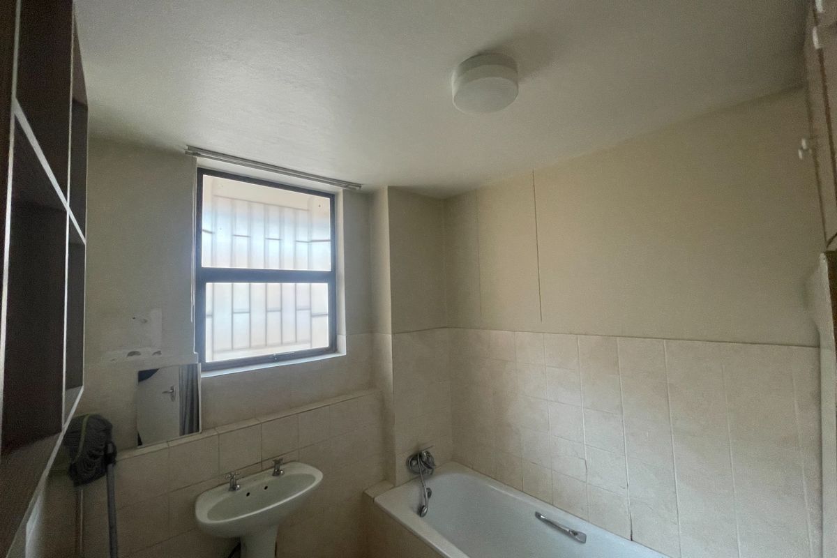 A functional bathroom featuring a pedestal washbasin, bathtub, and tiled splashback, with built-in shelving and security bars on the window.