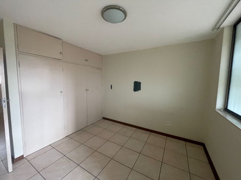 An empty bedroom featuring tiled flooring and built-in cupboards, requiring minor cosmetic updates to the wall finishes.
