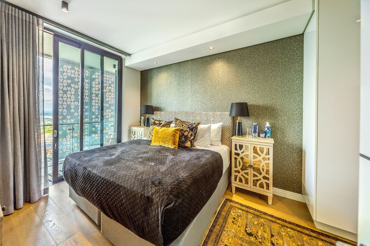 Modern bedroom featuring a textured feature wall, timber flooring, built-in wardrobe, and large sliding glass doors providing access to a private balcony.