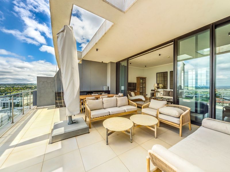 Spacious covered balcony featuring tiled flooring, glass balustrades, and seamless indoor-outdoor flow through large sliding glass doors, offering expansive views.