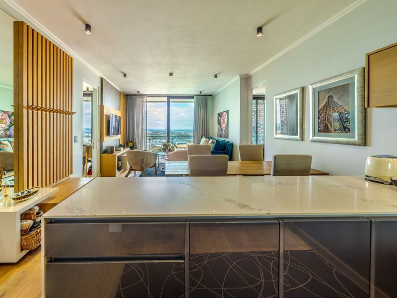 Modern open-plan living area featuring a sleek kitchen island with stone countertop, timber wall accents, and expansive sliding doors leading to a balcony view.