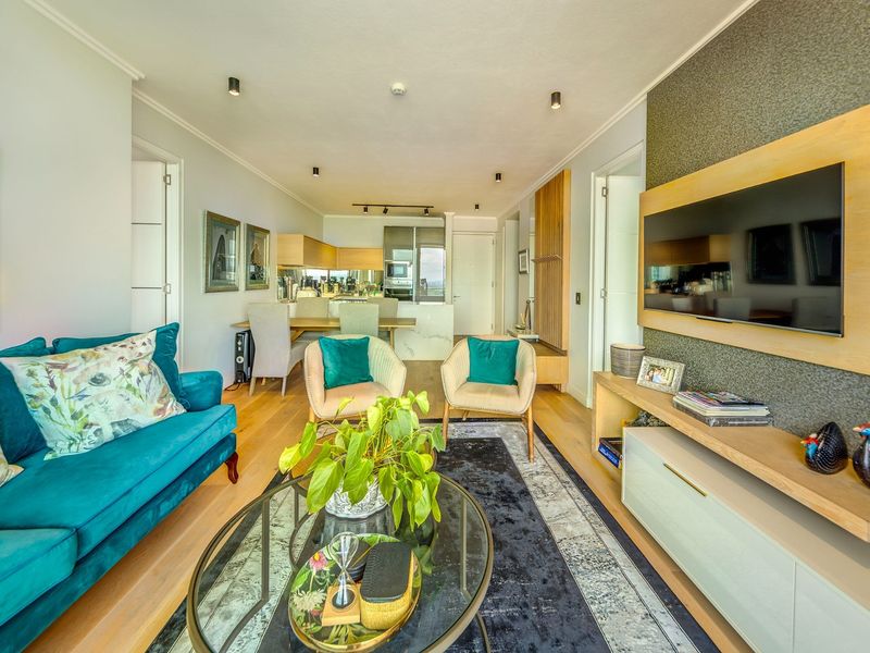 Modern open-plan living and dining area featuring timber flooring, recessed lighting, and a sleek kitchen with integrated appliances and stone island.