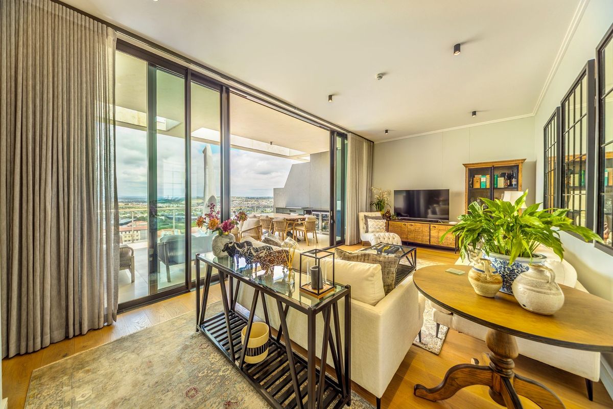 Spacious living area featuring high-quality hardwood flooring, recessed lighting, and expansive floor-to-ceiling sliding glass doors that open onto a covered balcony with scenic views.