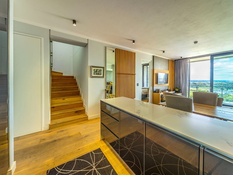 Modern open-plan living area featuring a sleek kitchen island, timber staircase, and floor-to-ceiling glass doors offering expansive views.