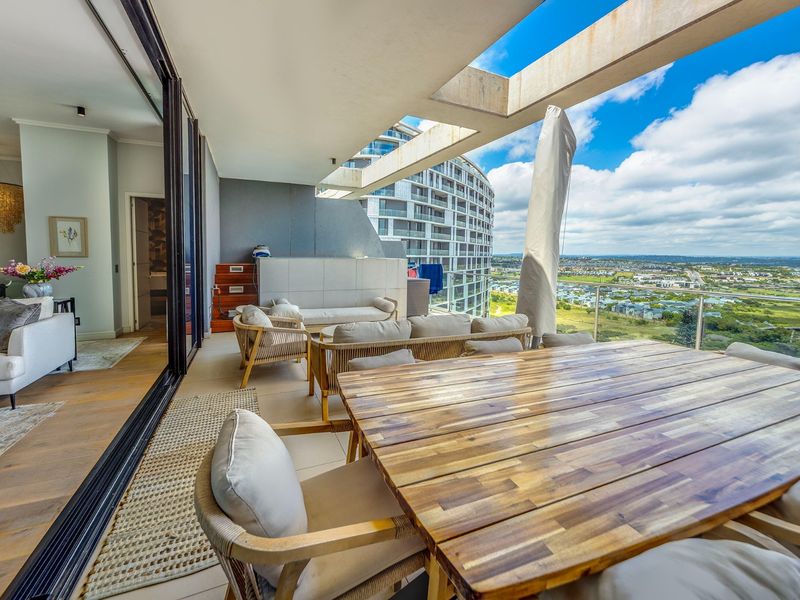 Spacious covered balcony featuring tiled flooring, a glass balustrade, and a concrete pergola, offering expansive views of the surrounding area.