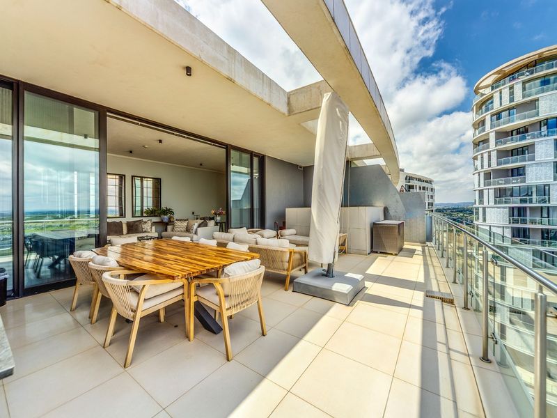 Spacious covered balcony featuring tiled flooring, a modern glass balustrade, and seamless indoor-outdoor flow through large sliding glass doors.