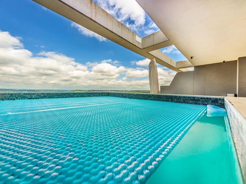 A modern elevated swimming pool area featuring a protective pool cover and a contemporary concrete pergola structure with expansive sky views.