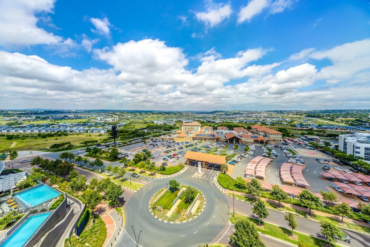An elevated aerial view of the apartment complex surroundings, featuring a roundabout, parking facilities, and communal swimming pool area.