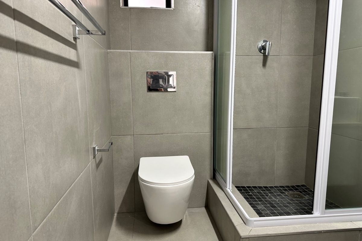 Modern bathroom featuring a wall-mounted toilet with concealed cistern, tiled finishes, and a glass-enclosed shower.