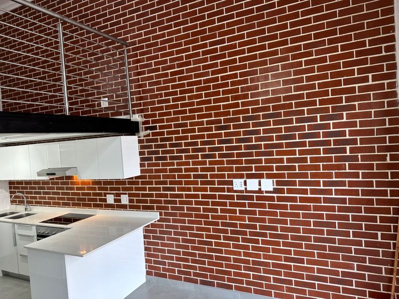 Modern kitchen featuring a striking exposed brick feature wall, sleek white cabinetry, stone countertops, and a stainless steel mezzanine balustrade.