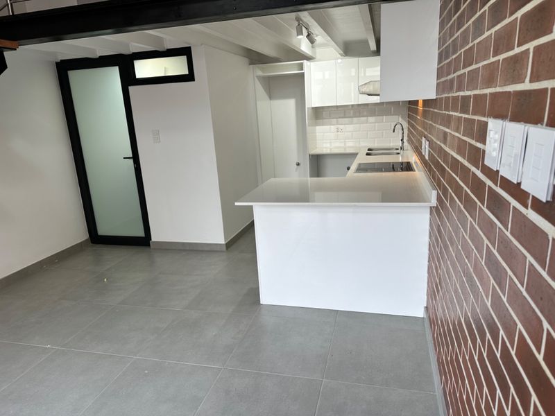 Modern kitchen featuring white cabinetry, stone countertops, integrated hob, and a striking exposed brick wall, set against neutral tiled flooring.