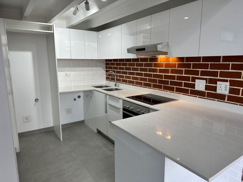 Modern kitchen featuring white gloss cabinetry, stone countertops, subway tile and brick backsplash, built-in oven, and electric cooktop with integrated extractor fan.