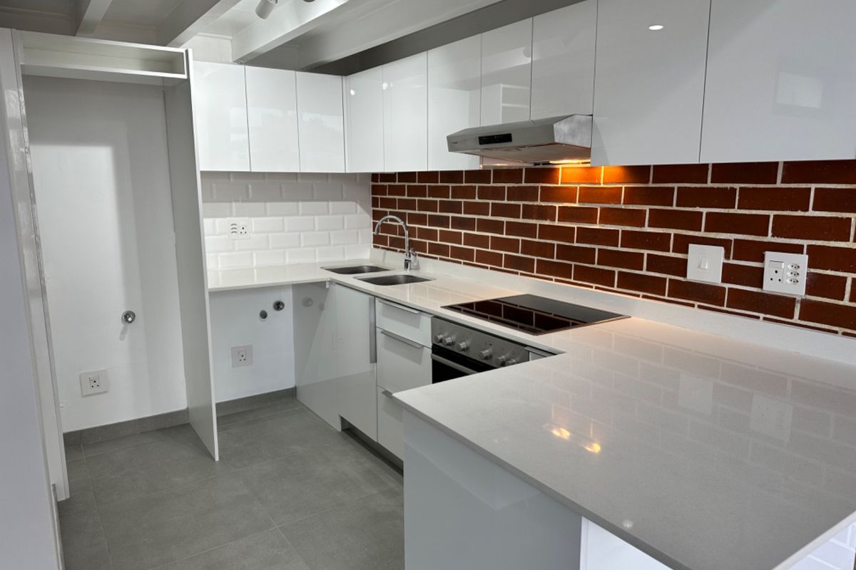 Modern kitchen featuring white gloss cabinetry, stone countertops, subway tile and brick backsplash, built-in oven, and electric cooktop with integrated extractor fan.