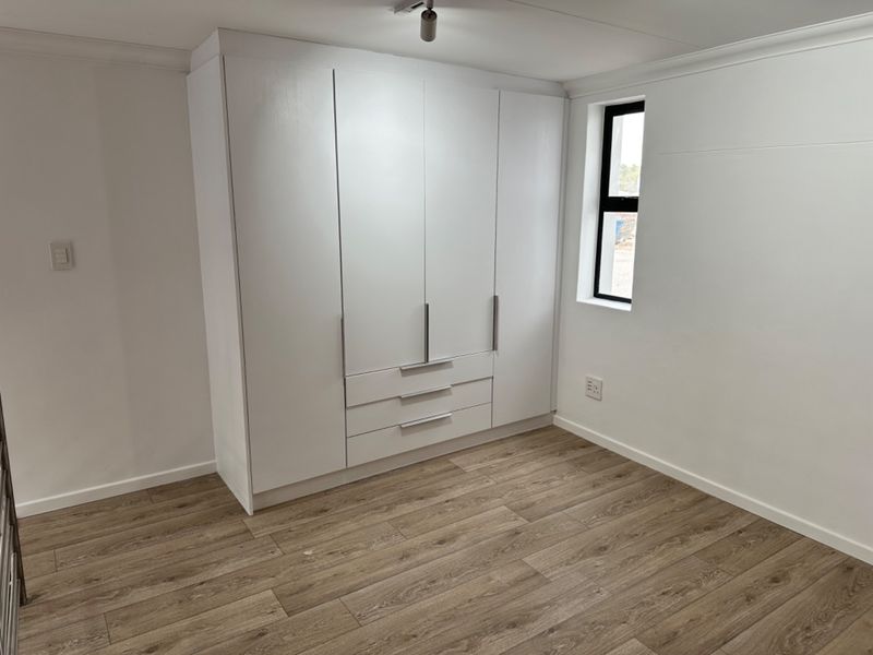 A clean, empty bedroom featuring modern laminate flooring, white walls, and a large built-in wardrobe with integrated drawers.