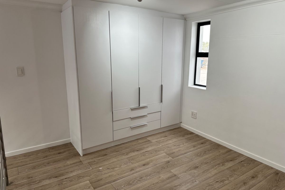 A clean, empty bedroom featuring modern laminate flooring, white walls, and a large built-in wardrobe with integrated drawers.