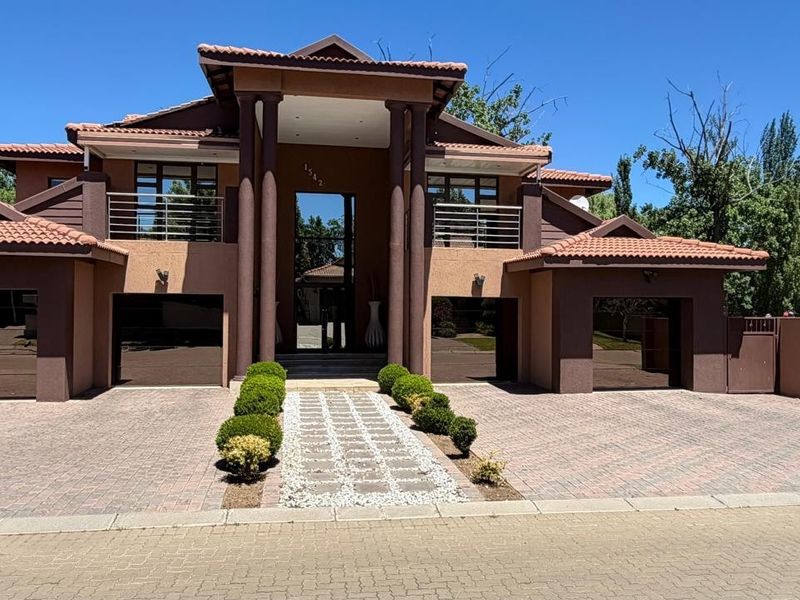 A well-maintained double-story residence featuring a triple garage, paved driveway, stone pathway, and a prominent entrance with decorative pillars and upper-level balconies.