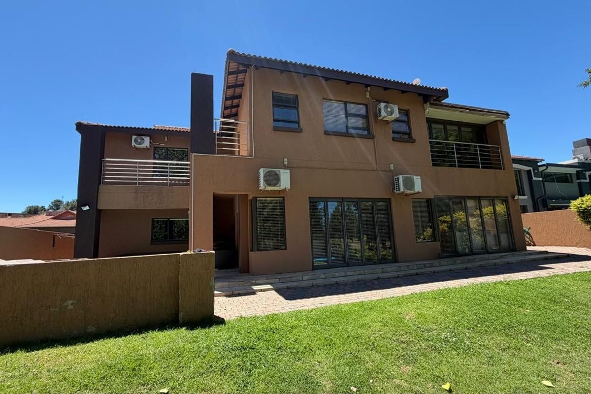 Rear view of a multi-story house featuring a paved patio, lawn, balconies with metal railings, and multiple air conditioning units.