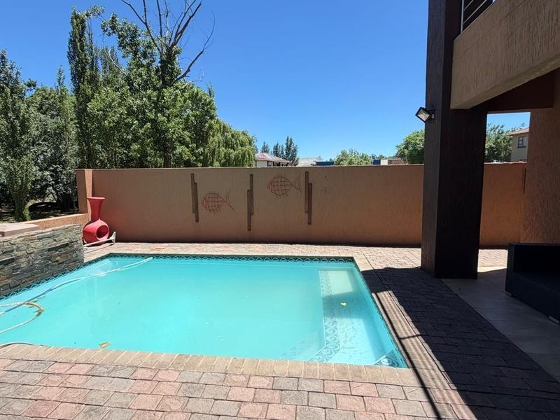 Outdoor pool area featuring a paved deck, stone-clad water feature, and a covered patio space, set against a private boundary wall.