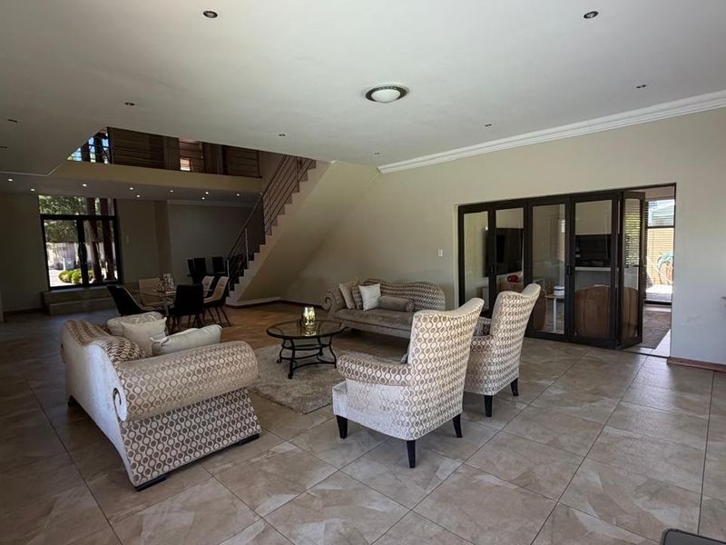 Spacious open-plan living area featuring tiled floors, recessed lighting, and a staircase with a modern metal railing leading to an upper level.