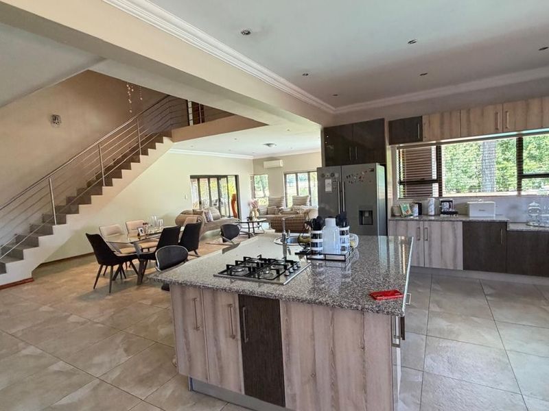 Spacious open-plan living area featuring a modern kitchen with a granite-topped island, gas hob, and a striking staircase with a stainless steel balustrade.
