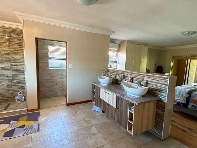 Spacious bedroom featuring an open-plan en-suite bathroom with a double vanity, vessel sinks, and a separate walk-in shower area.