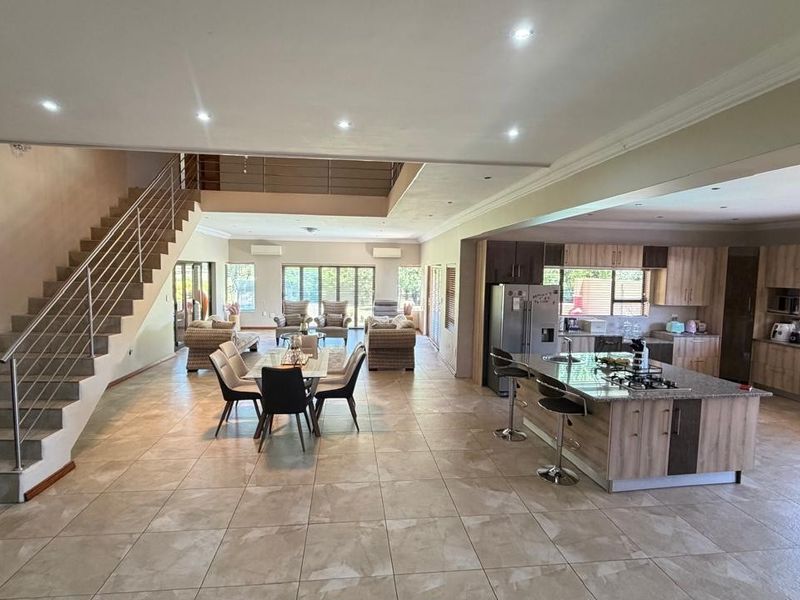 Spacious open-plan living area featuring a modern kitchen with a central island, dining space, and a prominent staircase with a sleek stainless steel balustrade.
