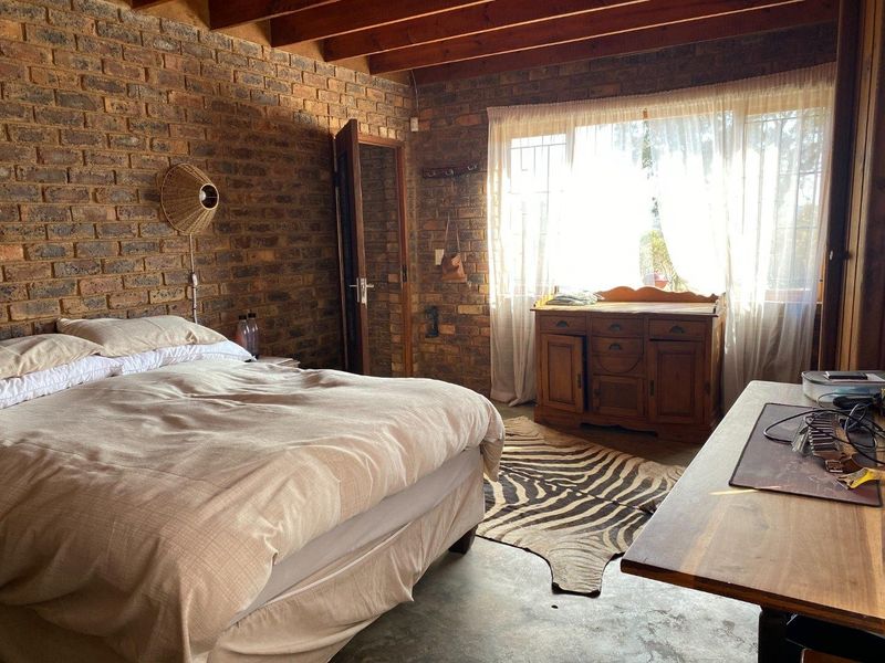 Rustic bedroom featuring exposed brick walls, timber ceiling beams, and polished concrete flooring, offering a warm and characterful living space.