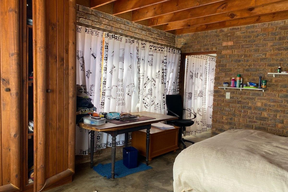 Rustic bedroom featuring exposed timber ceiling beams, face brick walls, concrete flooring, and a built-in wooden wardrobe.
