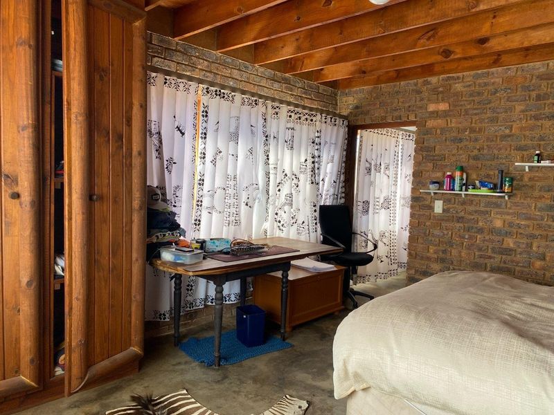 Rustic bedroom featuring exposed timber ceiling beams, face brick walls, concrete flooring, and a built-in wooden wardrobe.