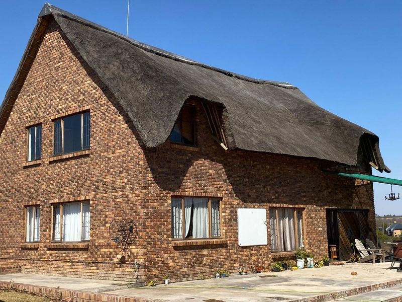 Rear view of a double-story face brick farmhouse featuring a traditional thatch roof and an adjoining concrete patio area.