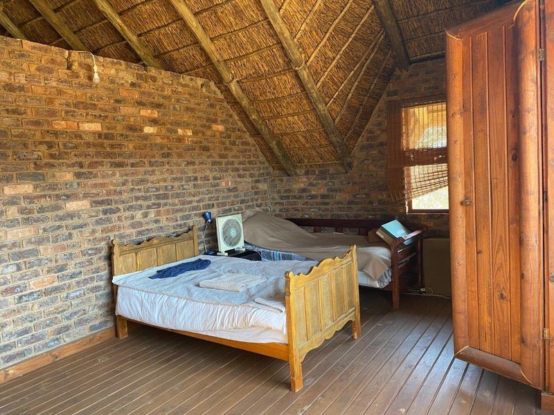 Rustic bedroom featuring exposed brick walls, a traditional thatched roof, and timber flooring, offering a cozy farm-style atmosphere.