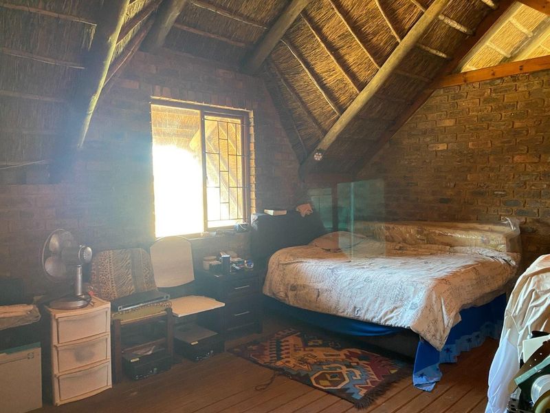 Rustic bedroom featuring exposed brick walls, a traditional thatched roof with timber rafters, and timber flooring, offering a unique farm-style aesthetic.