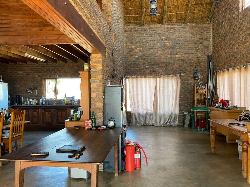 Spacious open-plan living and kitchen area featuring rustic exposed brick walls, high thatched ceilings with timber beams, and durable concrete flooring.