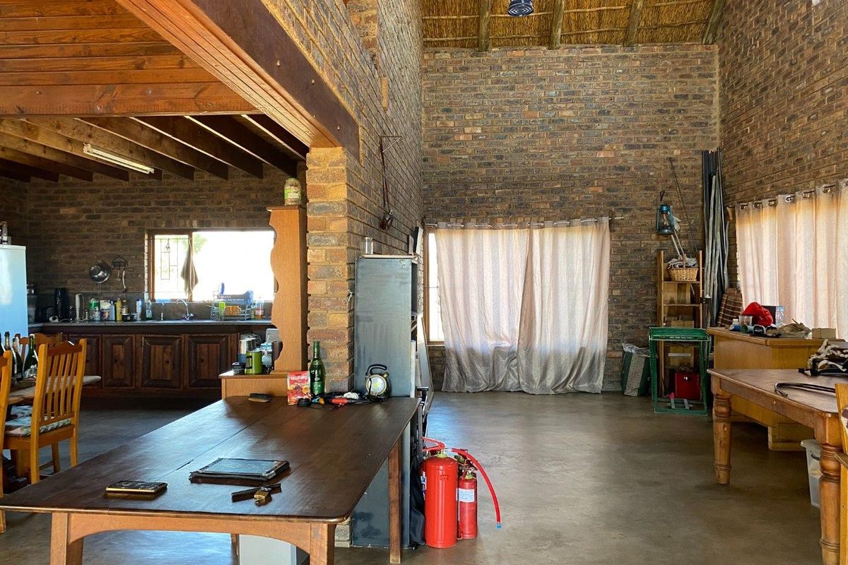 Spacious open-plan living and kitchen area featuring rustic exposed brick walls, high thatched ceilings with timber beams, and durable concrete flooring.